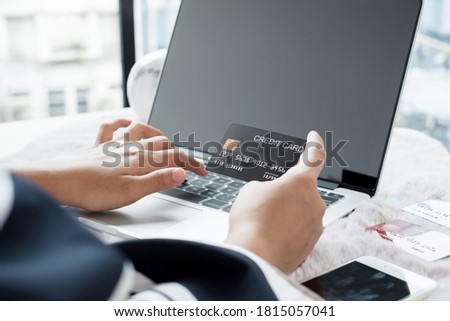 The businesswoman's hand is holding a credit card and using a laptop for online shopping and internet payment in the office.
