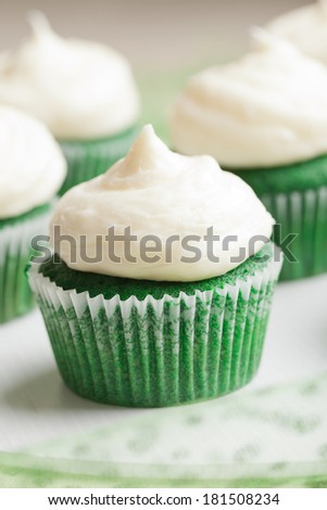Vertical macro shot of St. Patrick's Day green velvet cupcakes piped with a decadent cream cheese frosting - think red velvet cake green!