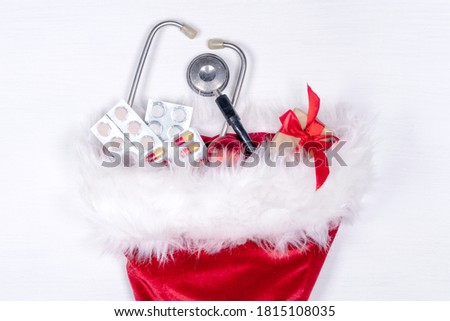 Medical Christmas card with pills, gift present box, stethoscope on white wooden background. Copyspace. Medicine new year flatly.