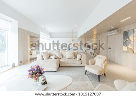 trendy modern interior design of a large studio in white and beige colors with large floor-to-ceiling windows. area of ​​white kitchen with an island and a recreation area Royalty-Free Stock Photo #1815127037