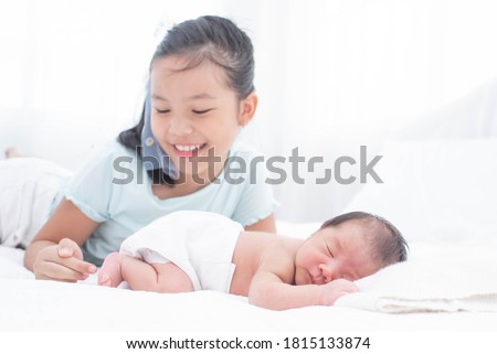 little sister hugging her newborn brother. toddler kid meeting new sibling. love, trust and tenderness. cute girl and new born baby boy relax in a white bedroom. family with children at home.