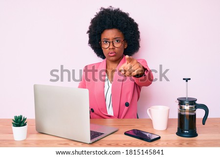 Young african american woman working at desk using computer laptop pointing with finger to the camera and to you, confident gesture looking serious 
