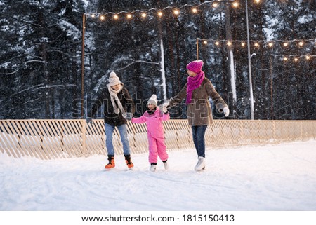 christmas, family and leisure concept - happy mother, father and daughter at outdoor skating rink in winter