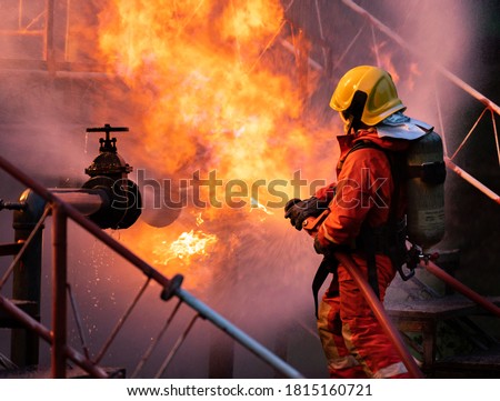 Firefighter using water fog type fire extinguisher to fighting with the fire flame from oil pipeline leak and explosion on oil rig and natural gas station. Firefighter and industrial safety concept. Royalty-Free Stock Photo #1815160721
