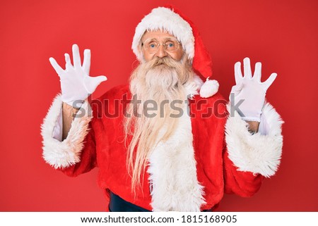 Old senior man with grey hair and long beard wearing traditional santa claus costume showing and pointing up with fingers number nine while smiling confident and happy. 