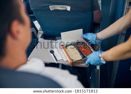 Close up portrait of air stewardess serving box of food for male passenger in protective gloves to prevent covid virus affection in airplane cabin Royalty-Free Stock Photo #1815171812
