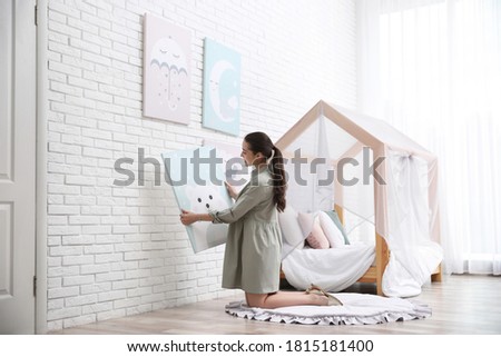 Decorator hanging picture on white brick wall. Children's room interior design