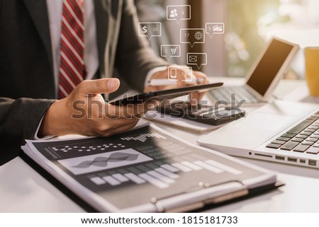 Business man using digital tablet analyzes business data, busy working on laptop computer with smart phone and business report on office desk.