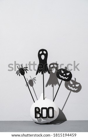 Halloween home decorations. Painted white pumpkin and black scary Halloween shadow puppets on sticks on a light gray background. Copy space, vertical orientation.