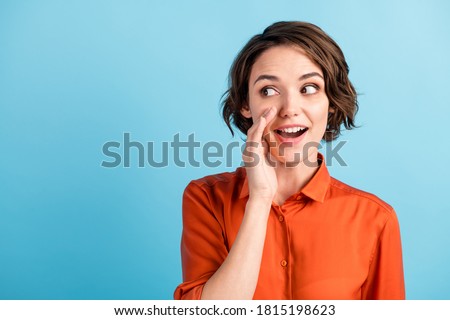 Closeup photo of attractive funny lady cute bobbed hairdo hold arm near mouth look side empty space tricky tell secret best friend chatterbox wear orange shirt isolated blue color background Royalty-Free Stock Photo #1815198623