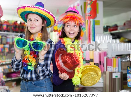 Portrait of happy comically dressed girls joking in festive accessories shop