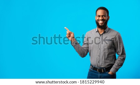 Cool Offer Concept. Portrait Of Smiling Young Black Bearded Man Pointing Finger At Copy Space Isolated Over Blue Background. Cheerful Confident African American Guy Indicating Free Space, Banner