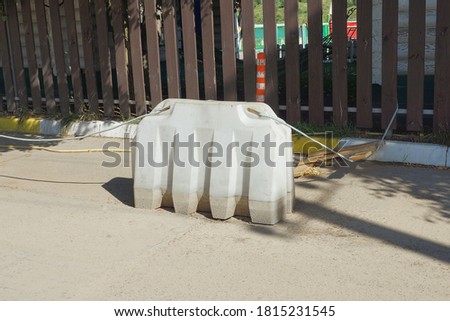 one white plastic barrier stands on gray asphalt near a brown wooden fence outside