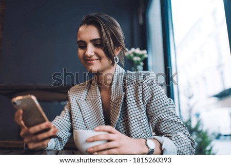 Successful Caucasian woman searching information via modern cellphone gadget using 4g wireless internet connection in cafe interior, carefree female messaging and networking during coffee time