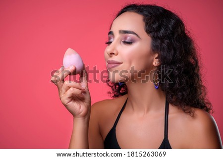 Beautiful young woman applying makeup using beauty blender sponge. Isolated over pink background