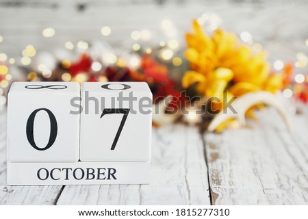 White wood calendar blocks with the date October 7th and autumn decorations over a wooden table. Selective focus with blurred background. 