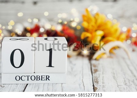 White wood calendar blocks with the date October 1st and autumn decorations over a wooden table. Selective focus with blurred background. 