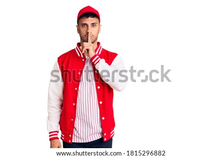 Young hispanic man wearing baseball uniform asking to be quiet with finger on lips. silence and secret concept. 