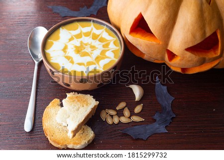 cream soup on the table, next to pumpkin, garlic, spoon, crouton, pumpkin seeds. happy Halloween
