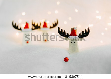 Three Christmas deer in red caps with pompoms. One in the foreground and his nose fell off and fell into the snow. The other two are among the snowdrifts. Postcard for congratulations. Background.
