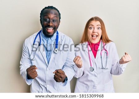 Young interracial couple wearing doctor uniform and stethoscope celebrating surprised and amazed for success with arms raised and open eyes. winner concept. 