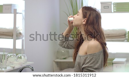 Young woman rinsing mouth with teeth rinse front mirror in bathroom before sleep. Healthy woman using dental rinse while morning care in bath room Royalty-Free Stock Photo #1815311912