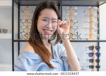 Asian beautiful young woman smiling, wearing and trying eyesight glasses in store. Sales, Discount and Optical Concept.