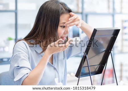 Asian beautiful woman trying to put contact lenses into her eyes and looking to the mirror. Lifestyle and Optic Concept. Royalty-Free Stock Photo #1815318479