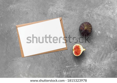 Blank paper card mockup with envelope and fresh figs. Gray concrete background. Company corporate identity template. Modern minimal still life. Top view, flat lay.