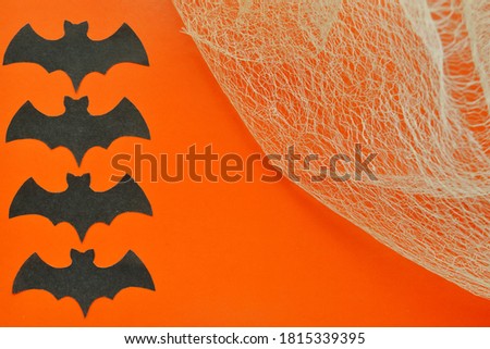 Black paper bats lie on orange background with cobwebs.