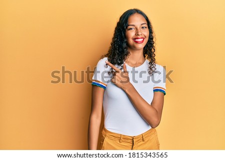 Young african american girl wearing casual clothes cheerful with a smile of face pointing with hand and finger up to the side with happy and natural expression on face 