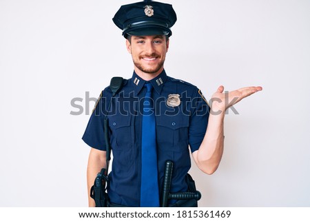 Young caucasian man wearing police uniform smiling cheerful presenting and pointing with palm of hand looking at the camera. 