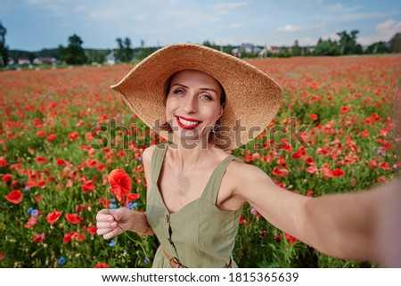 Summertime. Young woman in hat taking selfie on red poppy field.
