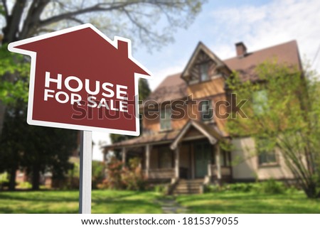 A red house shaped For Sale sign in front of a old style house. Real estate concept.