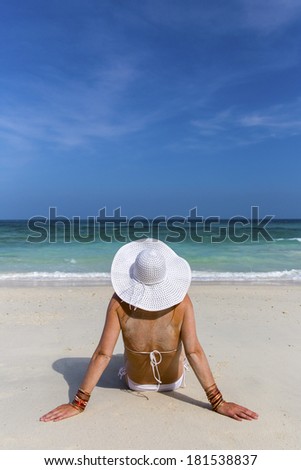 Summer vacation woman sitting on beach enjoying summer holidays looking at the ocean. Beautiful back side of model in bikini sitting down.