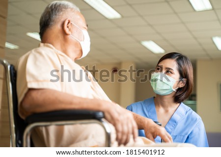 Healthcare concept, Asian nurse taking care and talking of mature male patient sitting on wheelchair in hospital. Woman and senior man wearing surgical face mask for protection of The COVID infection.