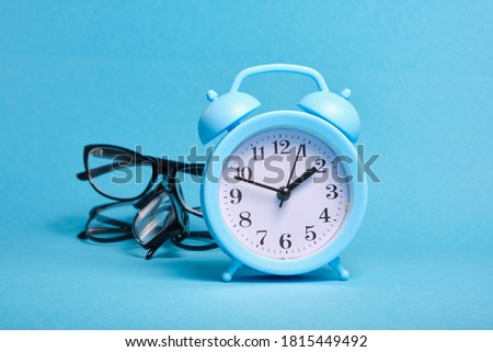 alarm clock and several different eye glasses on a blue background, glasses for children and adults, copy place, buy glasses concept