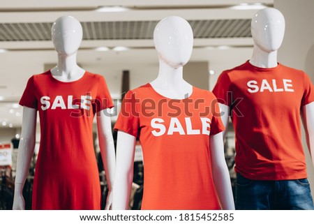 Fashion Mannequins in red T-shirts and text sale stand in shop window and attract shoppers. Black friday sale in casual store.