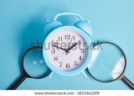 magnifiers and light blue alarm clock on a blue background