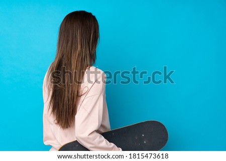 Teenager girl over isolated blue background with a skate in back position