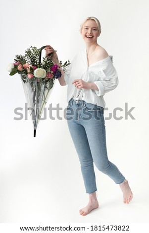 Cheerful pretty lady holding transparent parasol with flowers and smiling while standing against white background