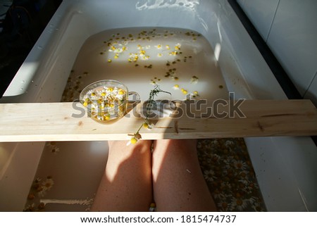 A Cup Of Fresh Hot Chamomile Tee With Flowers On The Wood Board On The Bathtub In The Bathroom. Summer Beauty Bath And Feminy Legs. Royalty-Free Stock Photo #1815474737