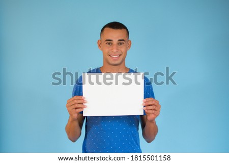 Handsome young man is holding a sheet of paper on blue background