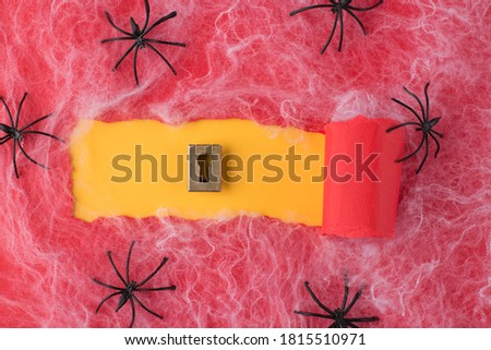 Top above overhead view photo of torn red paper and keyhole over yellow background with spiders and spiderweb