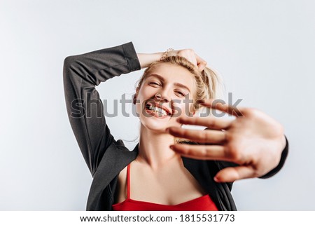 A beautiful blonde girl holds her hair and makes her own hairstyle with the emotion of happiness. Woman pulls her hand towards the camera on a gray isolated background for advertising. Nose piercing.