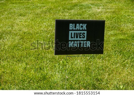 Black sign with blue writing on a green grass lawn that says black lives matter