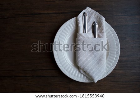 Clean cutlery in a cloth napkin lies on a plate against the background of a dark wooden table. Beautiful dinner setting for one person in a cafe. View from above. Copy space for text. Close-up.