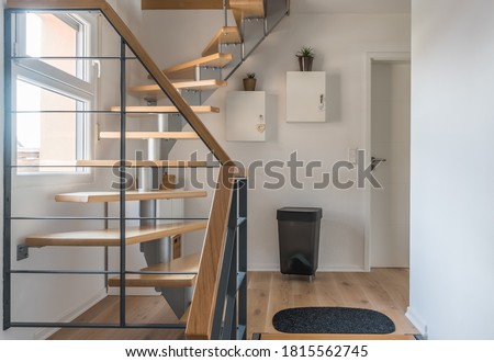 Staircase of a private house with modern stairs. Text on the small white heart is german and means "Live, Laugh, Love". Steel frame with wooden steps, white and gray walls, harmonious color concept. 