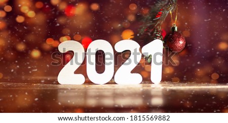 Christmas banner with white wooden number 2021.New Year magic background with holiday decorations: golden bokeh, falling snow, christmas tree, red ball which hang on a spruce branch. New year's eve  