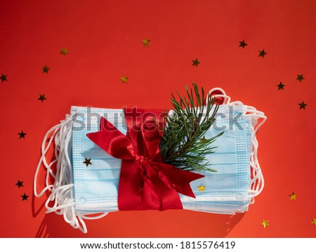 Hygienic face masks as a gift with a red ribbon, Christmas and New Year 2021 decor on a red background with space for text. Holidays self-isolation and coronavirus pandemic concept Royalty-Free Stock Photo #1815576419
